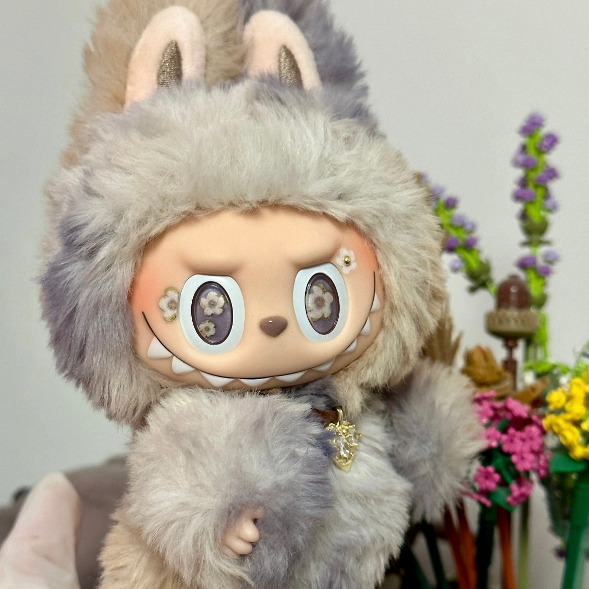 Plush toy with a furry hood resembling a creature, held by a person with a blurred background.