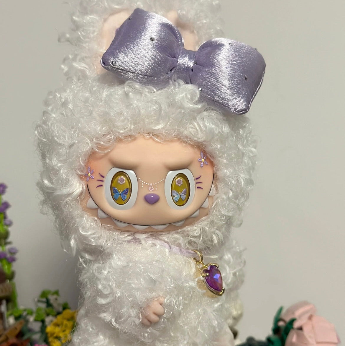 Stuffed animal with white fur and a large purple bow on a plain background